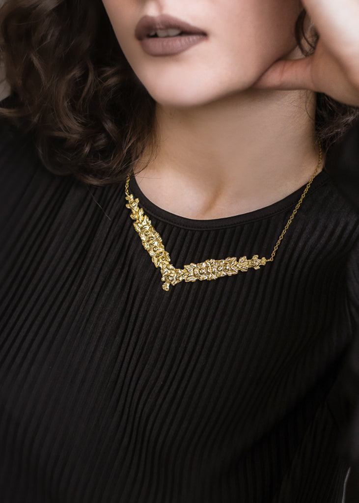 Brunette female in black blouse, wearing a gold, v shaped necklace and gold bracelets