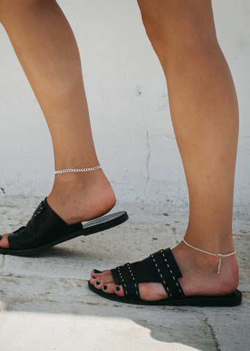 Female feet,with black sandals, and a silver, chain anklet, on either ankle.