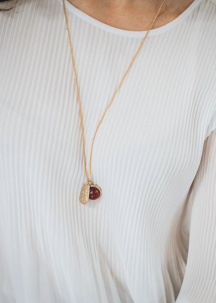 Cropped photo of an individual in a white blouse, wearing a gold necklace, with a brown carnelian semi precious stone