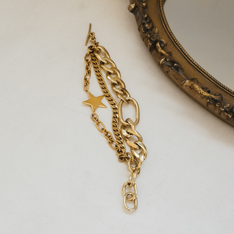 Orion. Gold, chain bracelet, placed open on a white surface, next to a wooden mirror