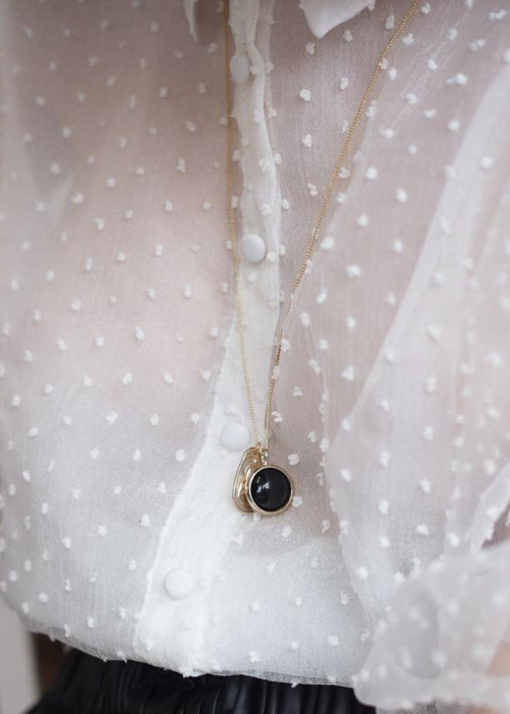 Individual in a white polka dot shirt, wearing a silver, long chain necklace with a black stone