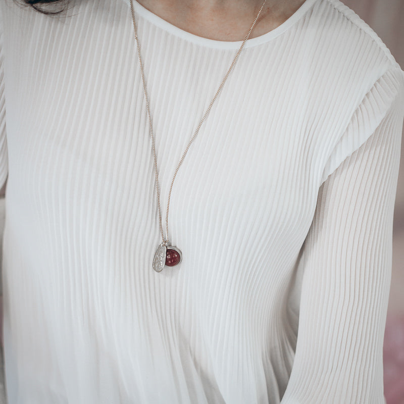 Cropped photo of an individual in a white blouse, wearing a silver, chain necklace with a brown carnelian semi precious stone