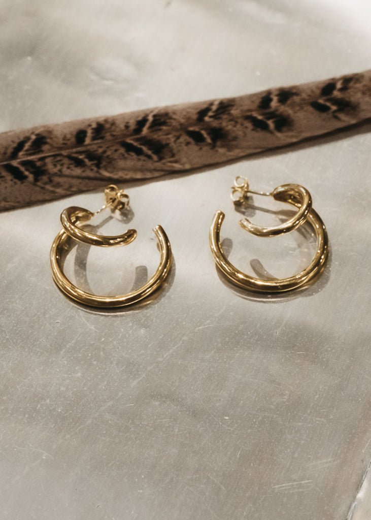 Double, round rod, loop earrings placed on an ivory surface, next to a long, brown feather