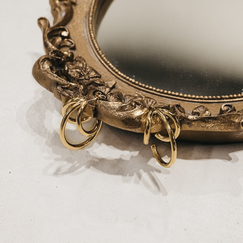 Pair of gold, Santiago, triple loop earrings, linked on the edge of a gold mirror