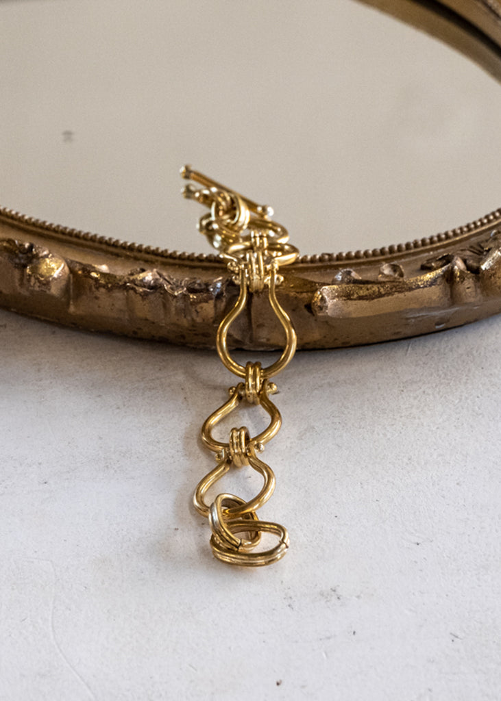 Unfastened, gold, link chain bracelet, placed half on a mirror, half on a white surface