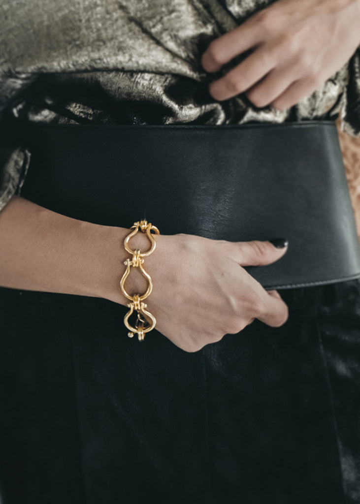 Female holding a black leather wallet with her right hand. On her wrist, a gold, link chain bracelet