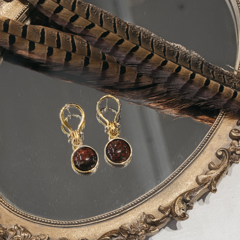 Pair of stunning, gold, unique link, pendant earrings with a round, brown carnelian stone, placed on a mirror
