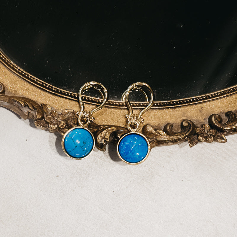 Pair of stunning, gold, unique link, pendant earrings with a round, turquoise stone, partially placed on a mirror