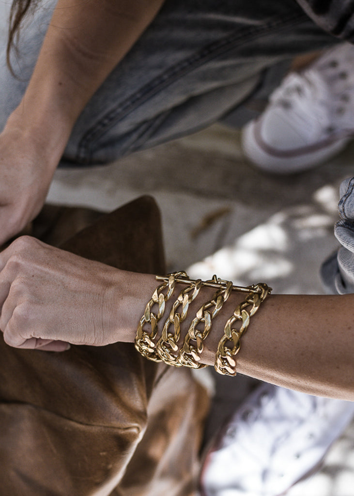 Woman's hands, closing a duffle bag. On her left wrist, she is wearing a Tetra, handmade, gold plated brass, chain bracelet.