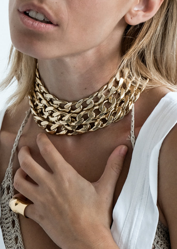 Blond woman in white blouse. She is wearing a Tetra, handmade, gold plated choker, and Punch, gold ring. Jewellery made in Athens Greece, by 3rd Floor Workshop