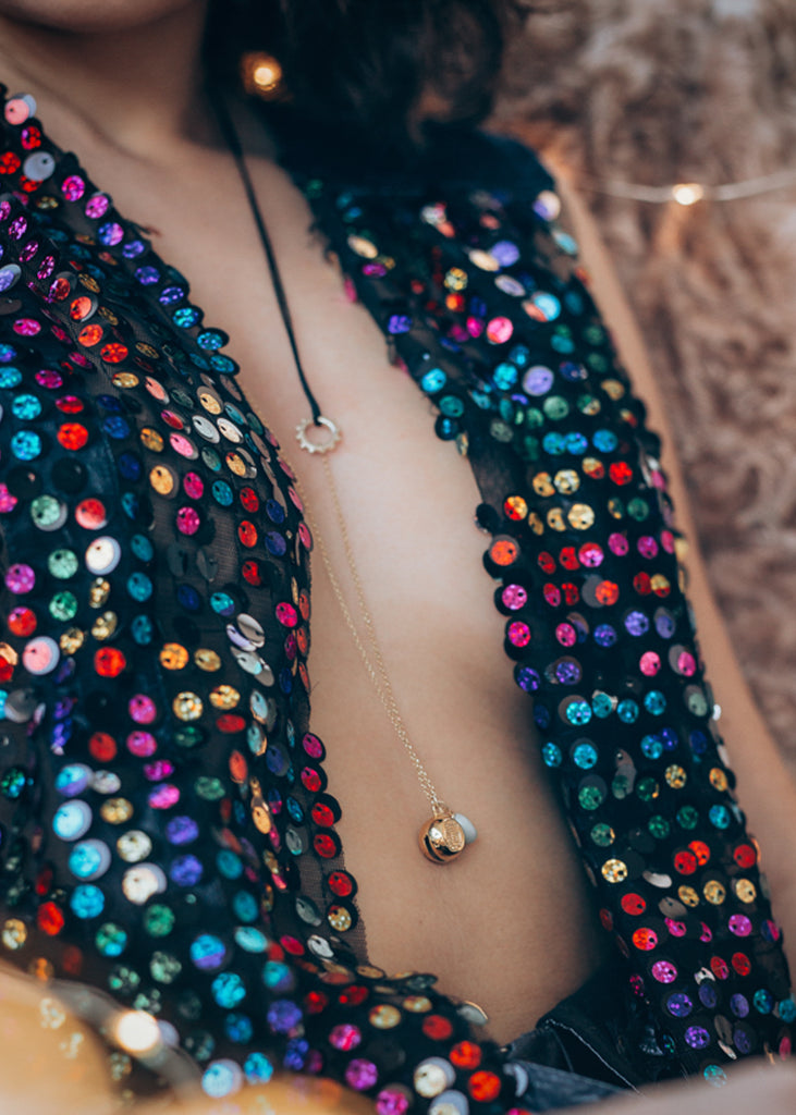 Close up of a female's bust, in a colorful, open shirt. She is wearing a long, handmade, Turtle Luck charm necklace
