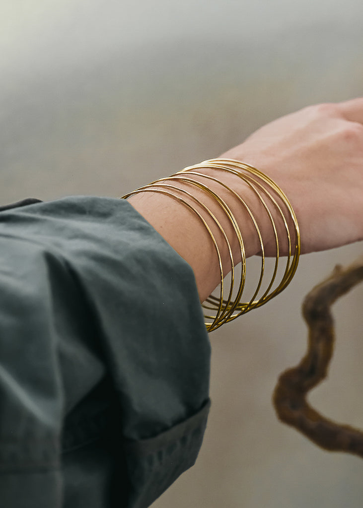 Female's hand as if it is reaching for something. On her wrist are many gold, thin bangle bracelets by 3rd Floor