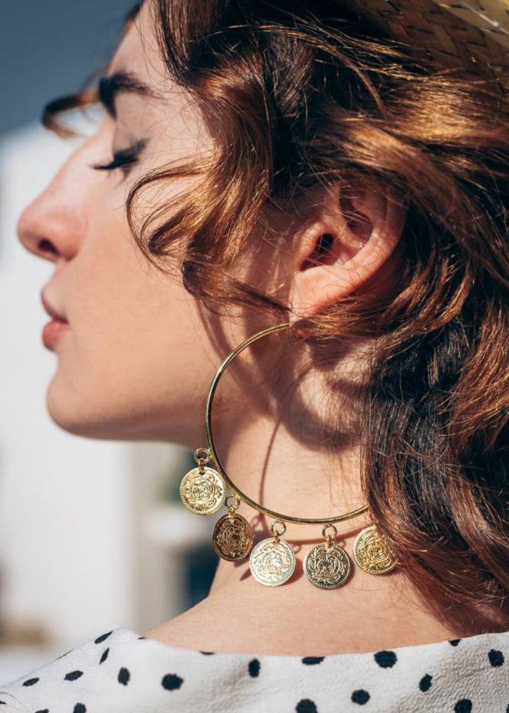 Brunette girl in profile. She is wearing a gold, loop earrings, with small, dangling coins
