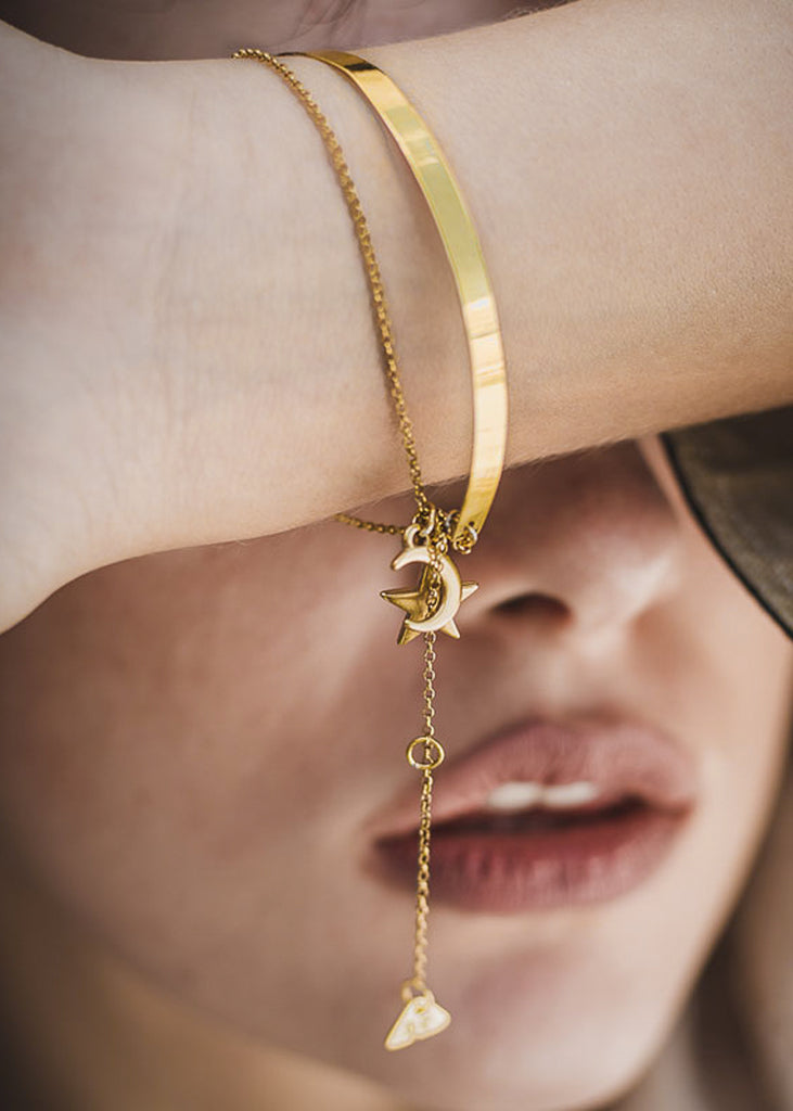 Close up of female's face, partially covered by her left forearm. She is wearing a double, gold plated, Night Sky bracelet