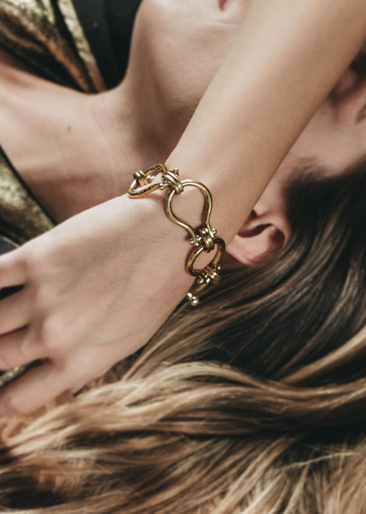 Female laying down. Her right hand over her face. On her wrist a gold, link bracelet