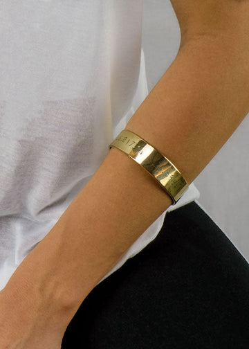 Close up of a forearm rested on a lap wearing a gold coordinates bracelet by 3rd Floor Handmade Jewellery