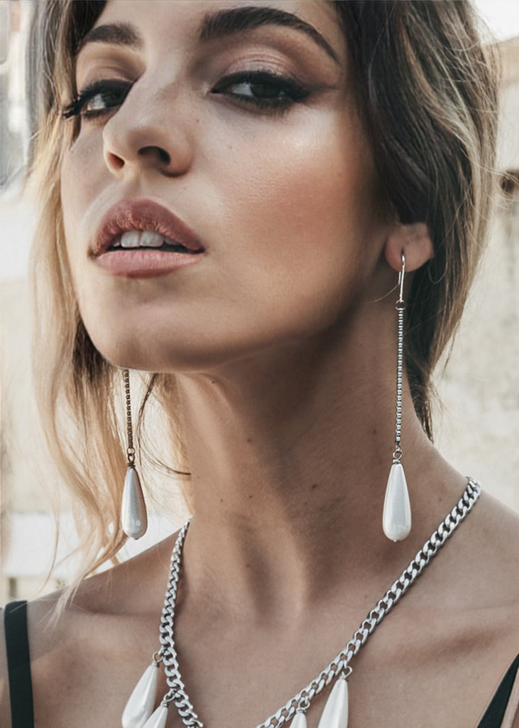 Female's close up on her face. She is wearing pearl drop, and chain pendant earrings