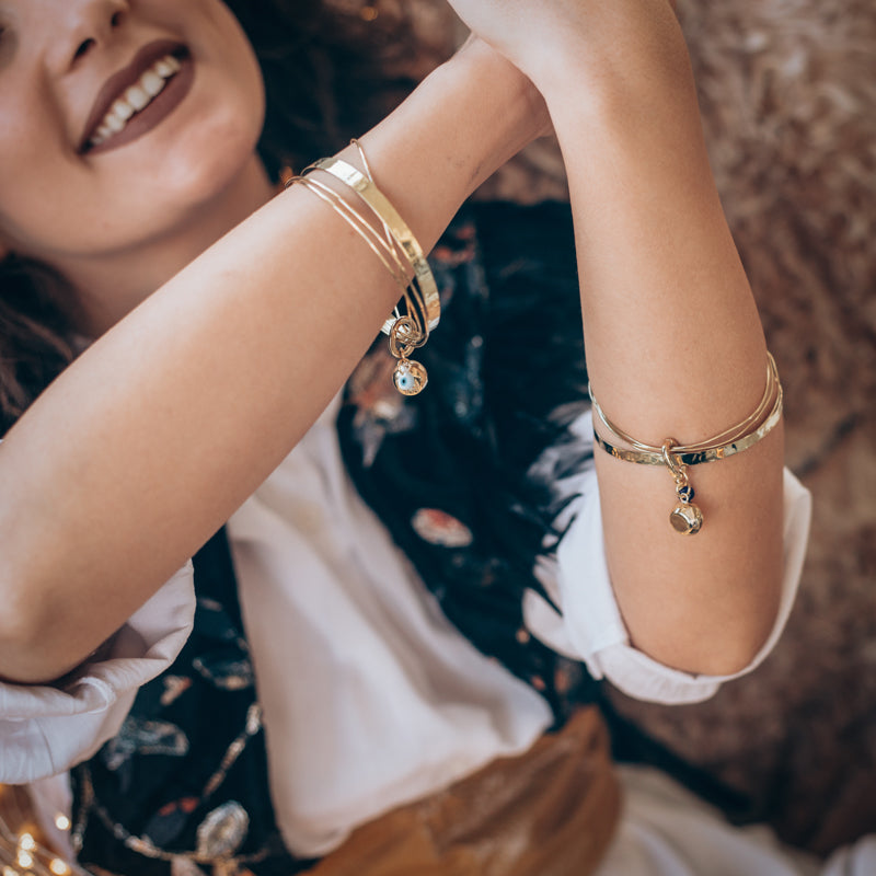 Happy, brunette girl, wearing handmade, gold, charm bracelets, on either wrist