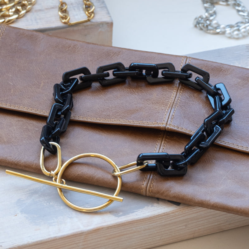 Black, square link necklace, with a gold, clasp buckle, placed on a brown wallet