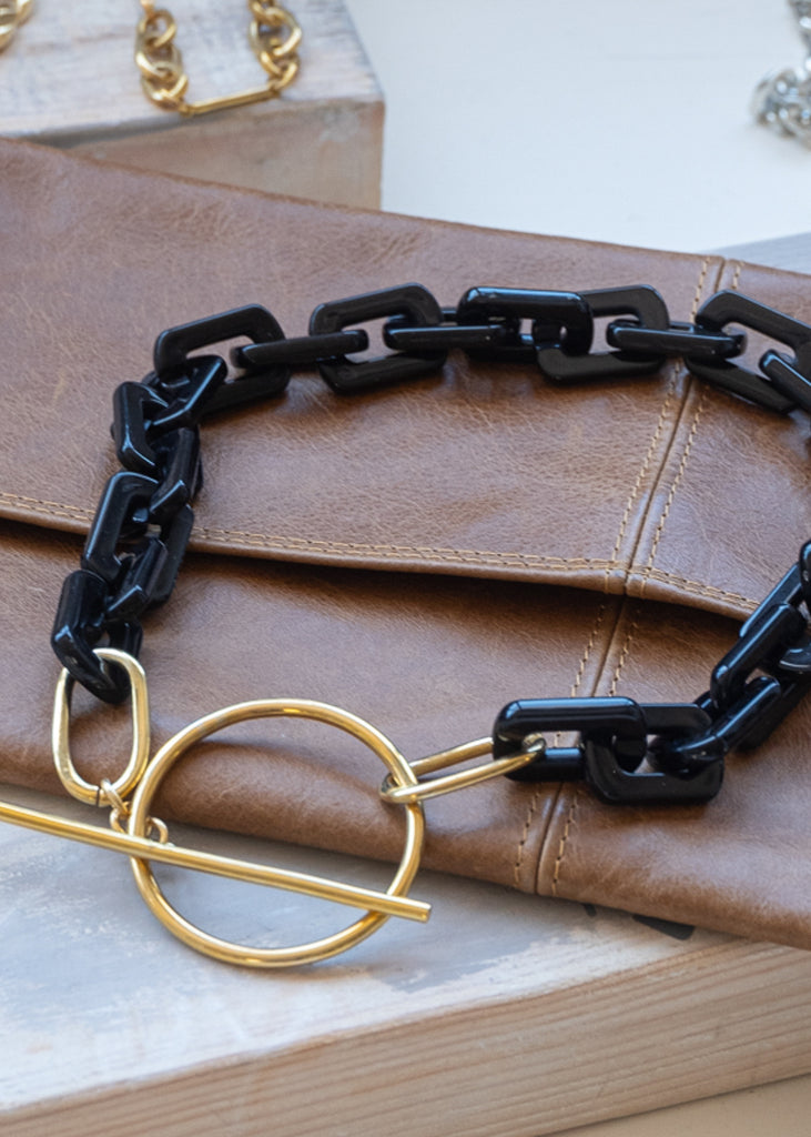 Black, square link necklace, with a gold, clasp buckle, placed on a brown wallet