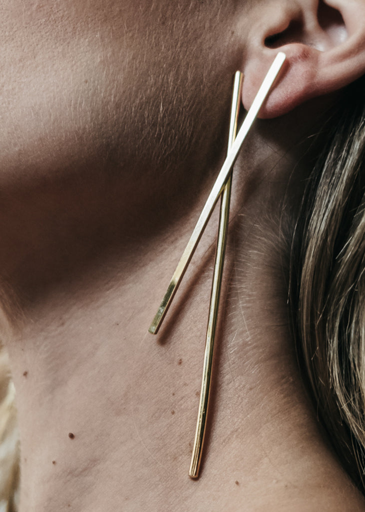 close-up, woman's face, wearing, a Pair of gold, long stick earrings, shaped like a linear X