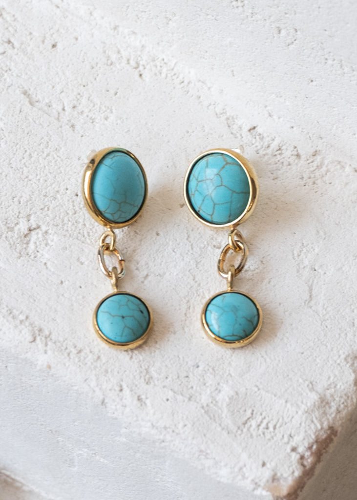 Gold pendant earrings, with two, uneven sized, encased, turquoise stones, held together by links