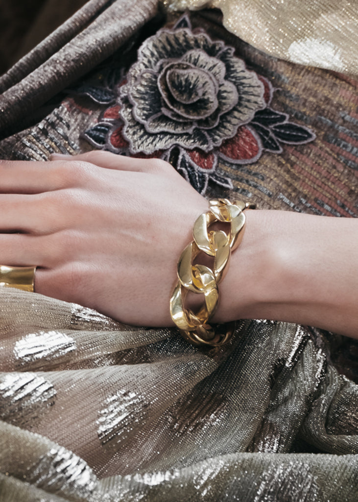 Beautiful, thin, female hand rested on impressive material. On her wrist a big, gold, chunky chain bracelet