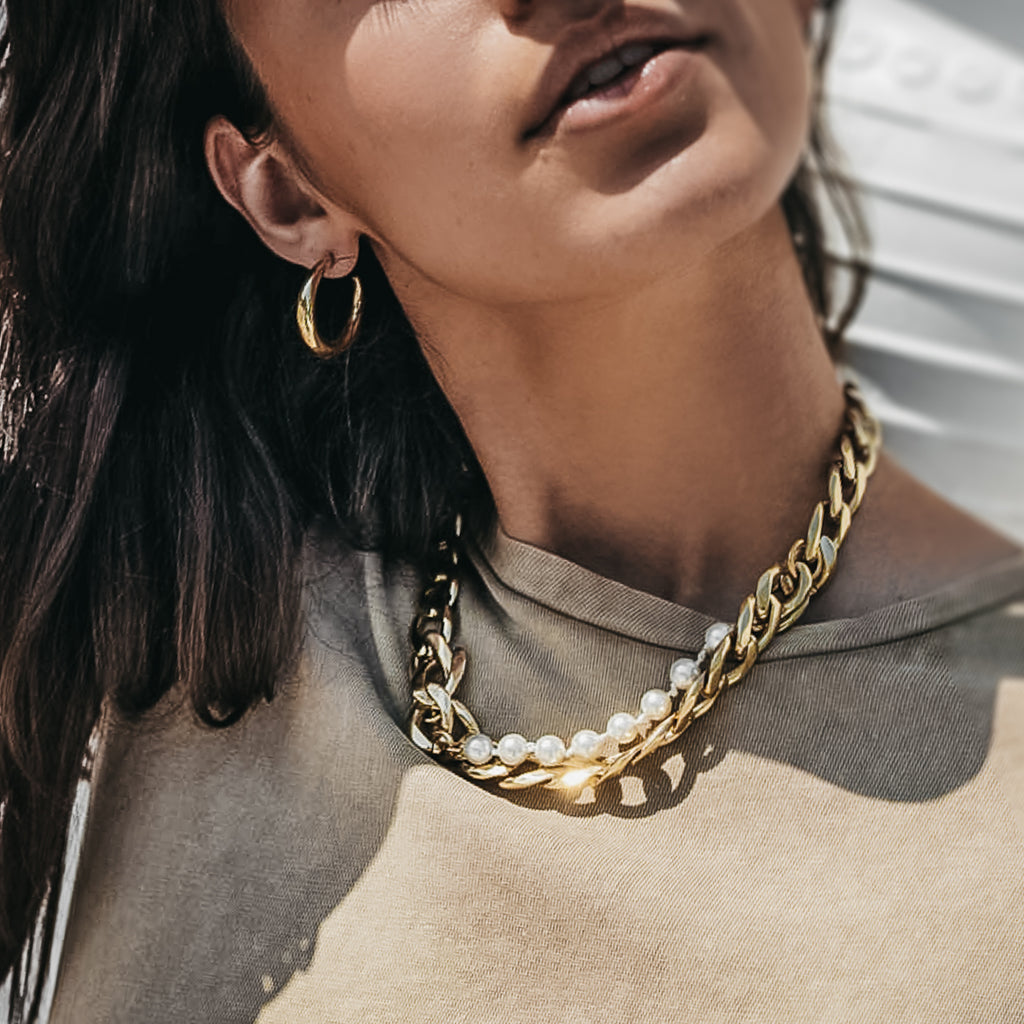 Young female is wearing a gold, link chain, and pearls necklace and a brown summer blouse