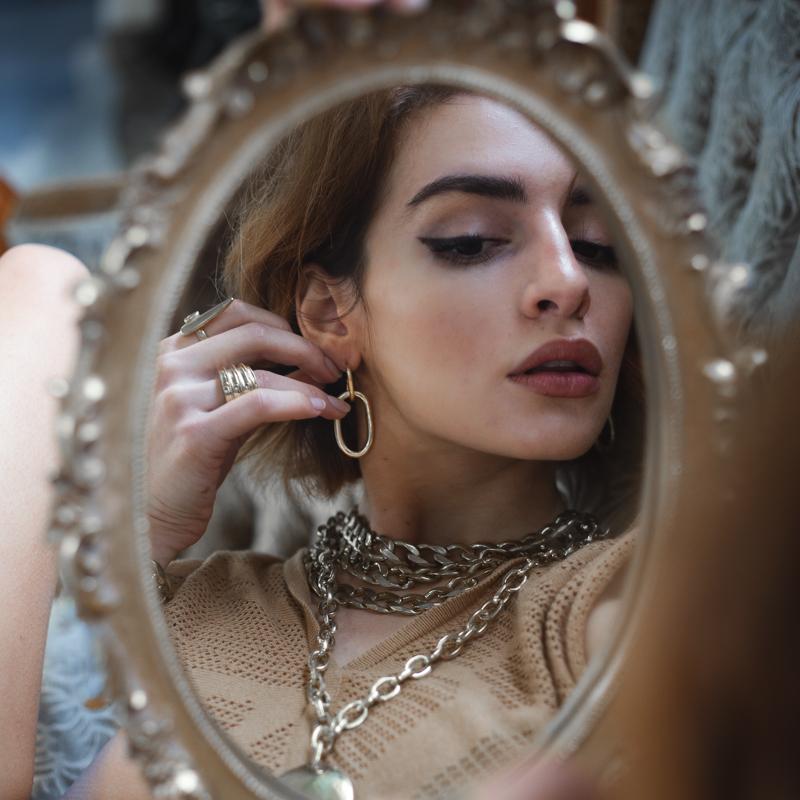 model looking to the mirror wearing Massive, loop chain earrings, in silver plated brass