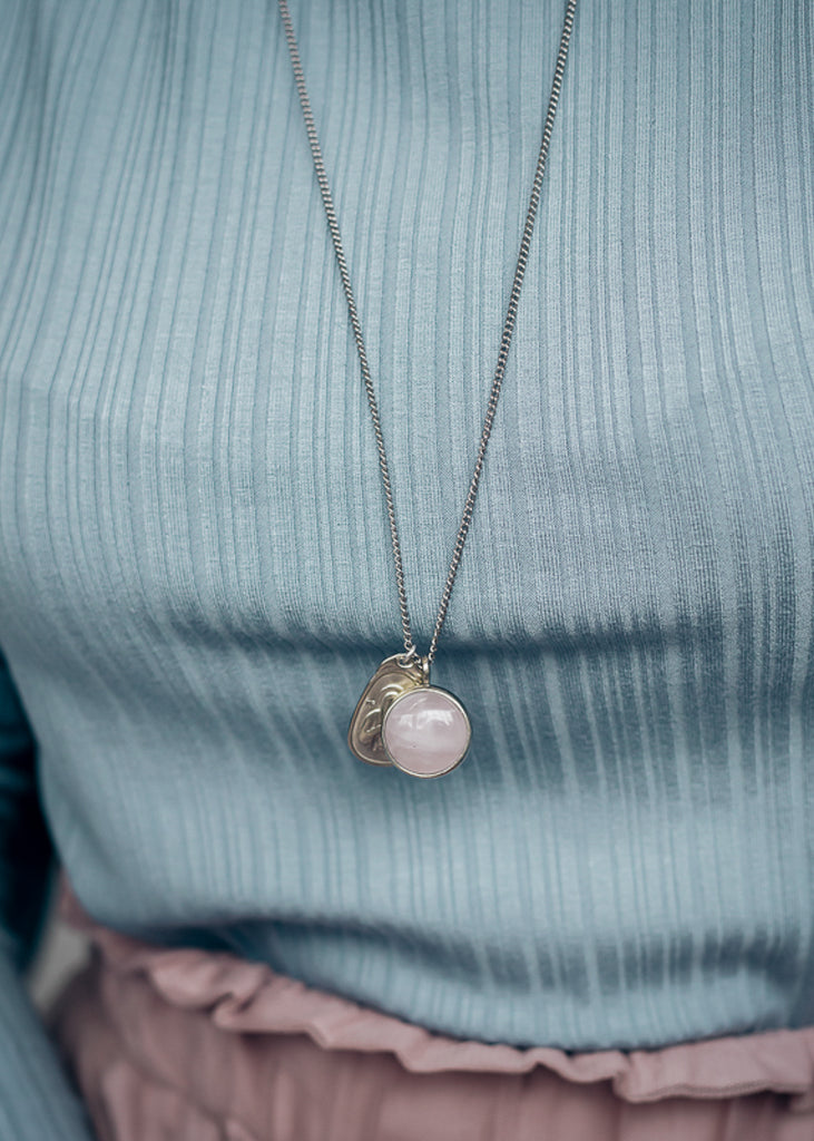  girl in a blue blouse. She is wearing a long, silver chain necklace with a silver plaque and a pink quartz stone