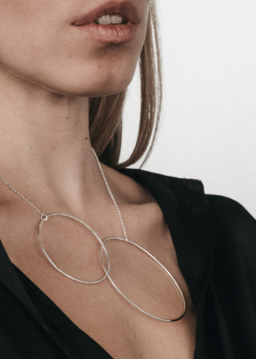 Lips to chest, cropped photo of female in a black unbuttoned shirt. She is wearing a silver chain necklace with two, interlocked links. By 3rd Floor Handmade Jewellery