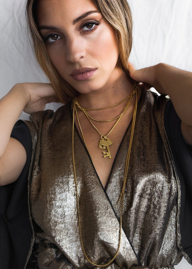 Female in beige, blouse. She is wearing a gold, triple chain, lock and key pendant 