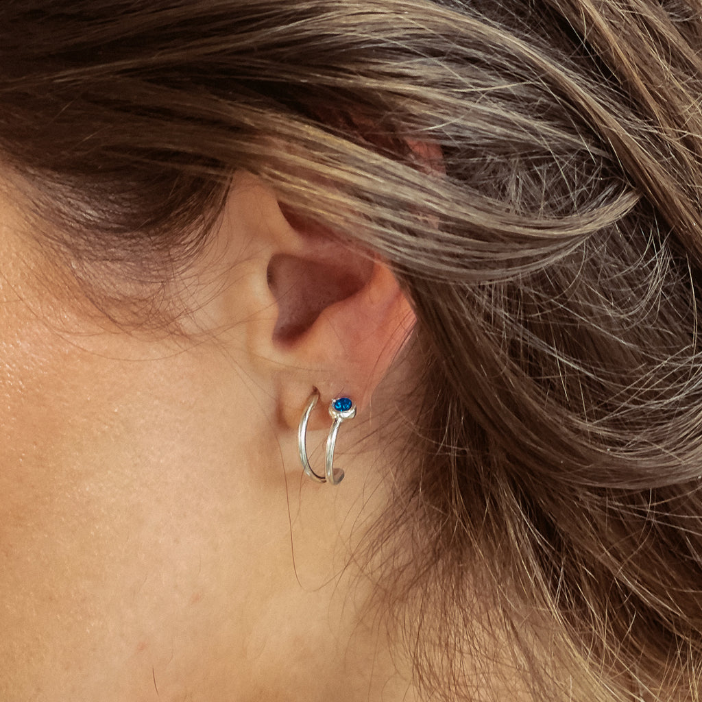 Χειροποίητο σκουλαρίκι ασημί με μία πέτρα Swarovski μπλε, φορεμένο στο αυτί μοντέλου.