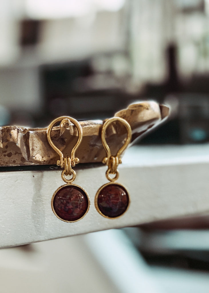Pair of stunning, gold, unique link, pendant earrings with a round, brown carnelian stone, placed on a mirror