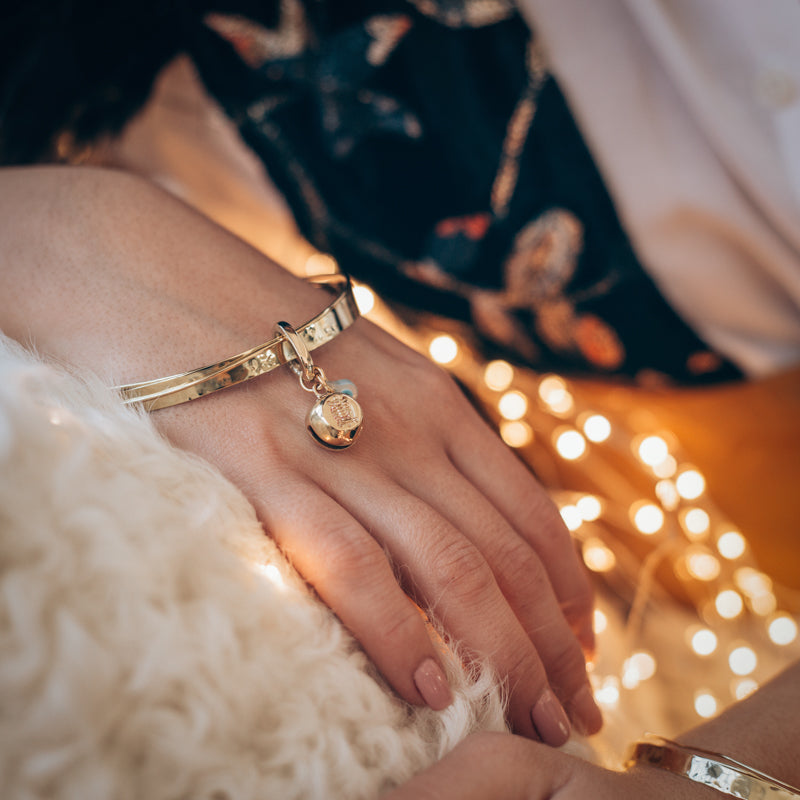 Close up of a female hand, rested on the arm of a couch. On her wrist she is wearing a handmade, gold, Turtle Luck bracelet