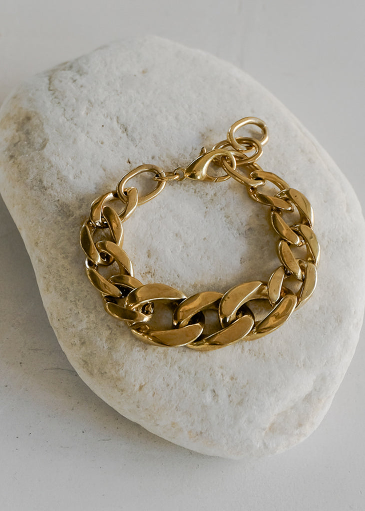 Mangata, gold, chunky chain bracelet, placed on a big, white stone.