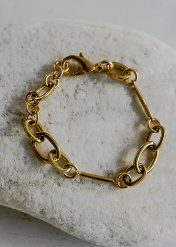 Gold, link and rod bracelet, placed on a white stone