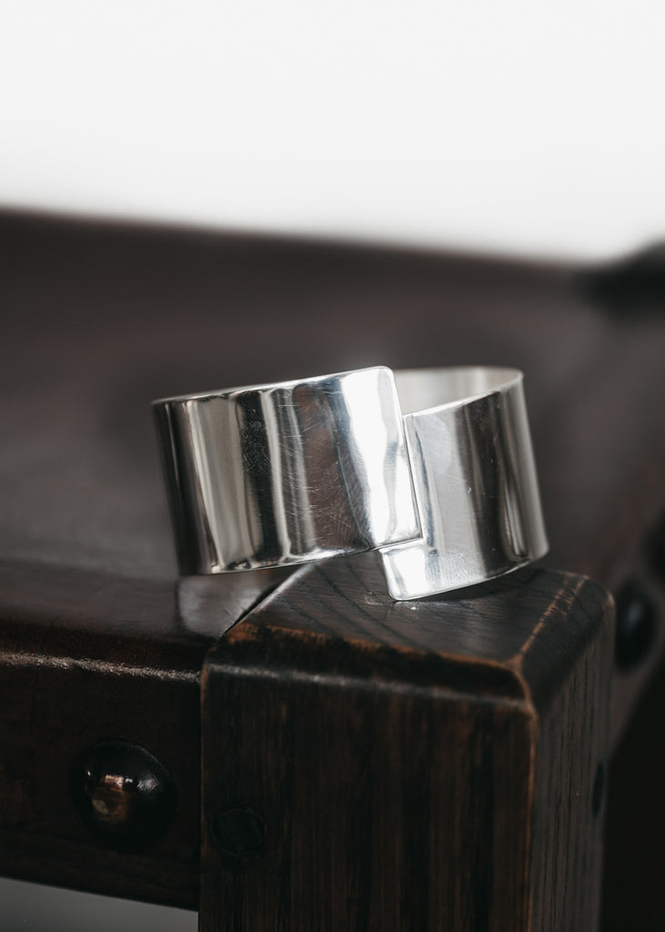 Wide, silver, cuff bracelet placed on a wooden surface. Koa cuff by 3rd Floor lab