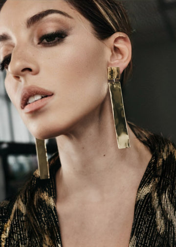 Close up of a female model's face. On her ears, dangle a pair of gold, Silhouette, pendant earrings by 3rd Floor