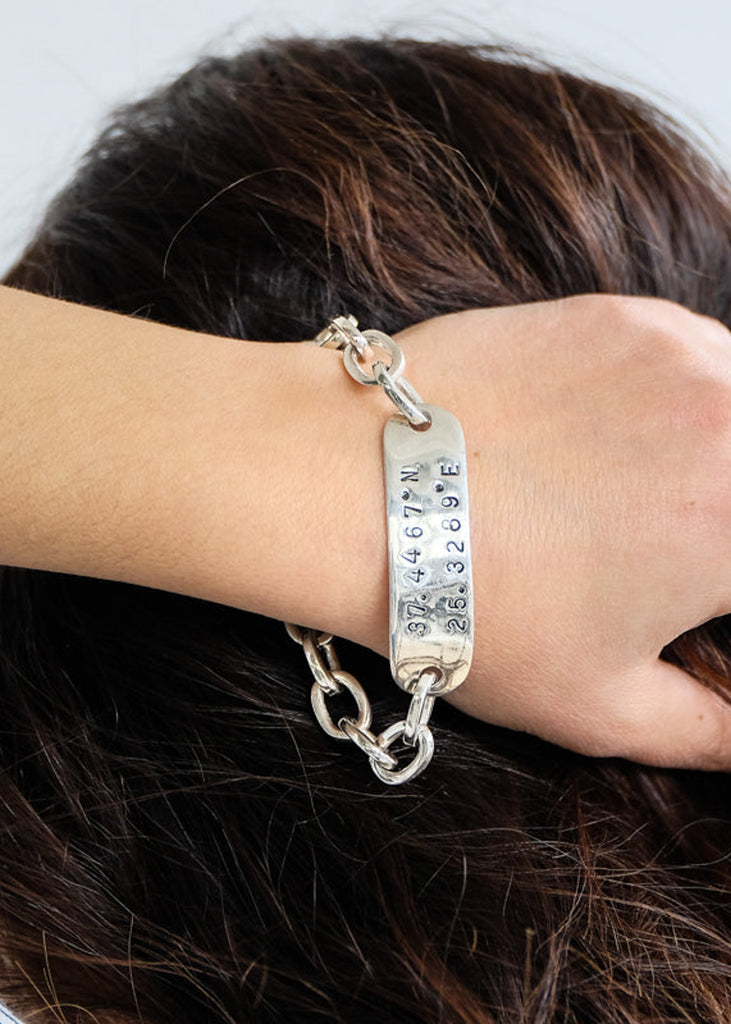 Brunette girl holding with her right hand the back of her head wearing a silver ID coordinates bracelet