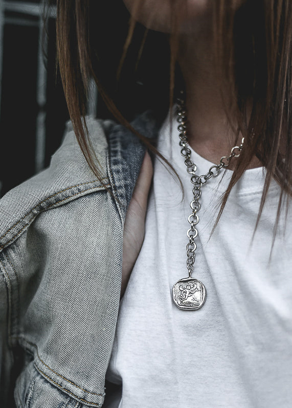 Girl in white t-shirt wearing a silver necktie neckpiece with a round charm with the greek god Hermes
