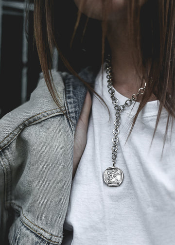 Girl in white t-shirt wearing a silver necktie neckpiece with a round charm with the greek god Hermes