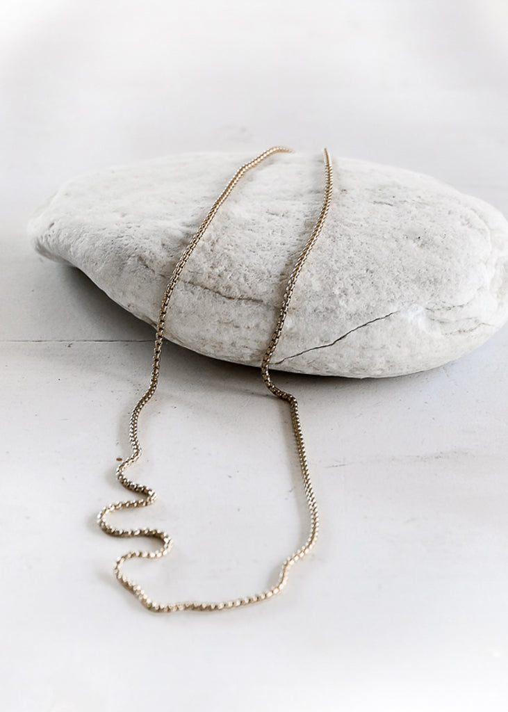 Silver, box chain necklace, half placed on a white stone